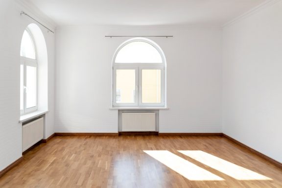 Heller, leerer Raum mit Holzfußboden und großen Fenstern.