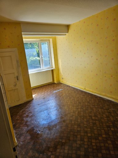 Leerer Raum mit gelben Wänden, einem Fenster und einem hellen Bodenbelag.