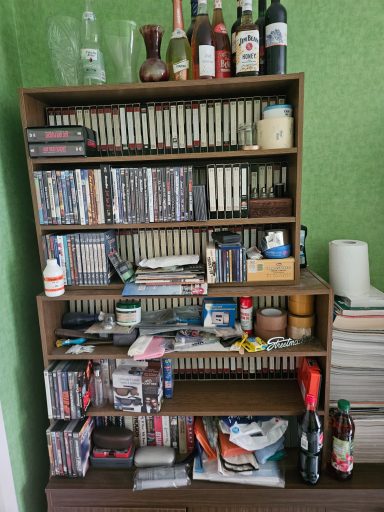 Ein Regal voller CDs, Flaschen und verschiedenen Gegenständen, teilweise unordentlich.