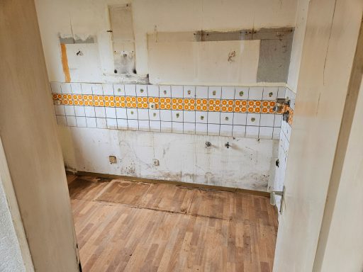 Leere Küche mit beschädigten Wänden und orangefarbenem Fliesenschnitt. Holzboden.