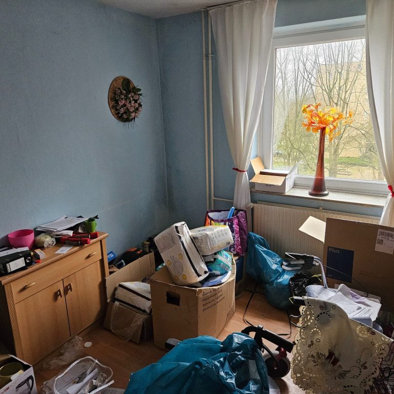 Unordentlicher Raum mit Umzugskisten, Gerümpel, Tüten und einem Fenster.