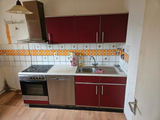 Küche mit roten Schränken, Edelstahl-Geräten und Fliesen in Orange und Weiß.