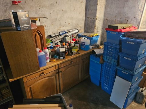 Keller mit Holzschrank, Werkzeug, Farben und blauen Kisten auf einem Tisch.
