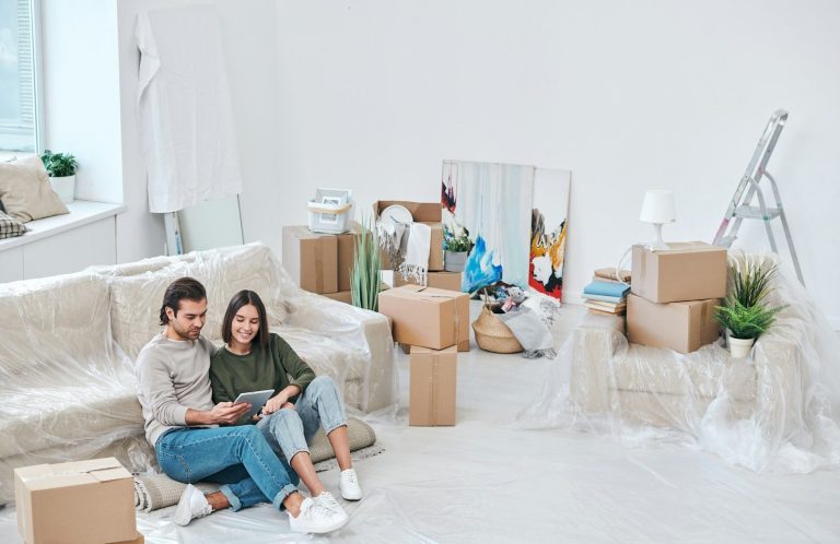 Junges Paar sitzt auf einem Sofa in einem ungestalteten Raum mit Umzugskartons.