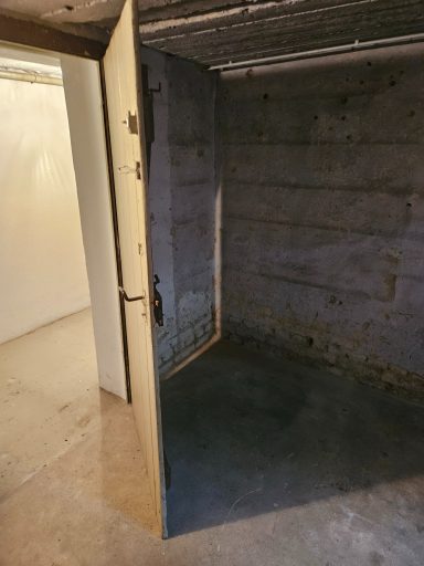 Ein offenes Türblatt führt in einen leeren, kahlen Raum mit Betonwänden.